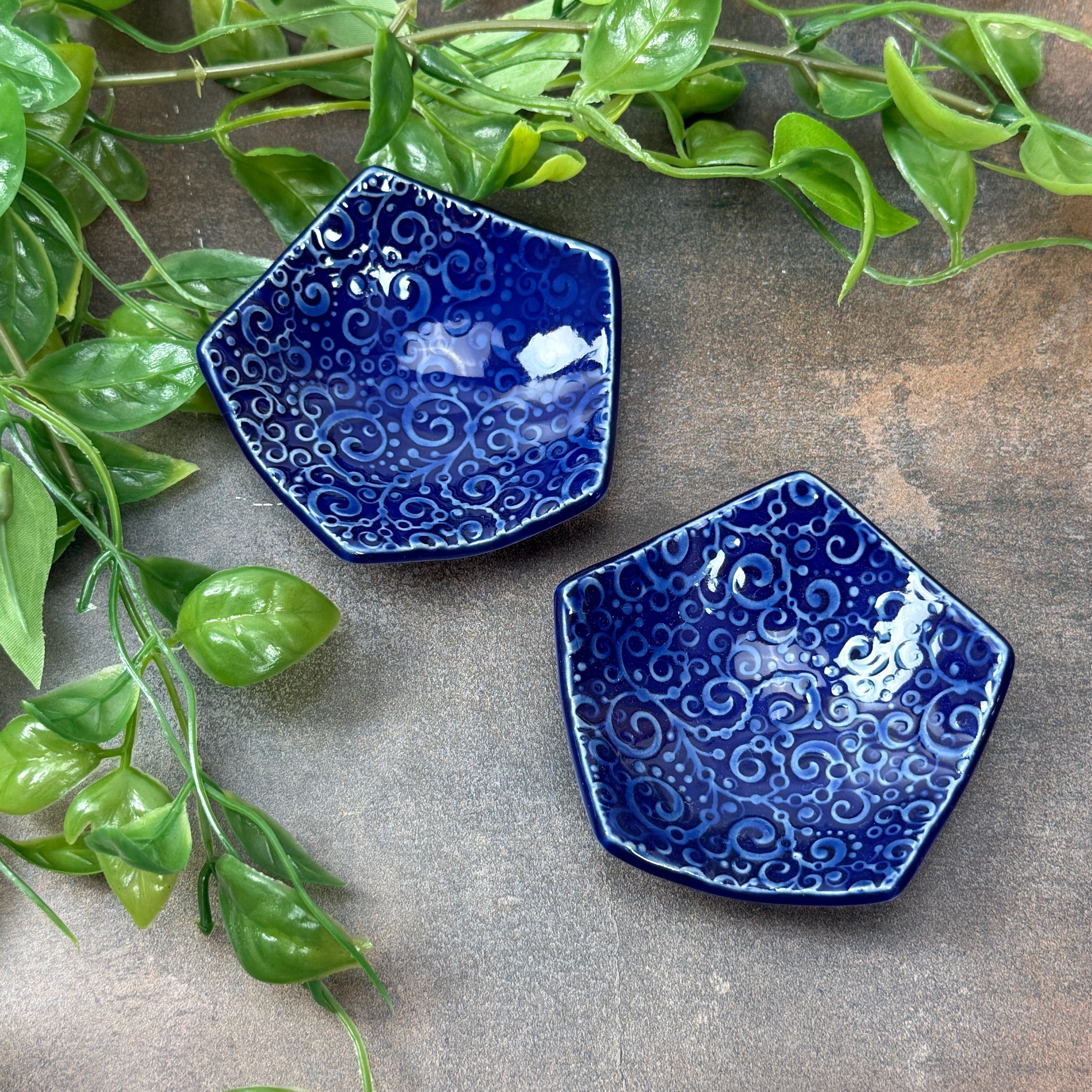 Two blue ceramic dishes with a textured pattern on a gray surface with green leaves.